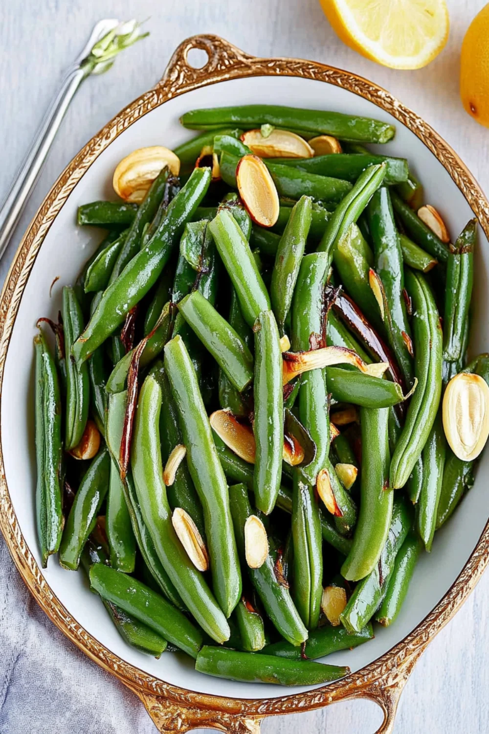A close-up of freshly made green beans almandine, topped with toasted almonds and served in a white bowl with a fork on the side.