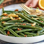 A close-up of freshly made green beans almandine, topped with toasted almonds and served in a white bowl with a fork on the side.