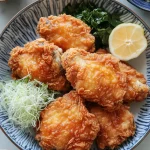 A close-up shot of crispy fried chicken pieces with a golden-brown, crunchy breading, revealing tender white meat inside.