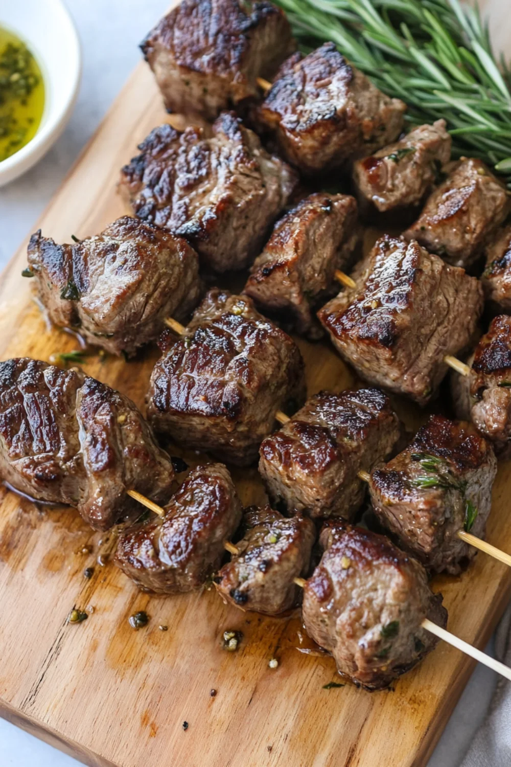 Grilled butter steak bites on skewers, garnished with chopped herbs and served on a wooden board.