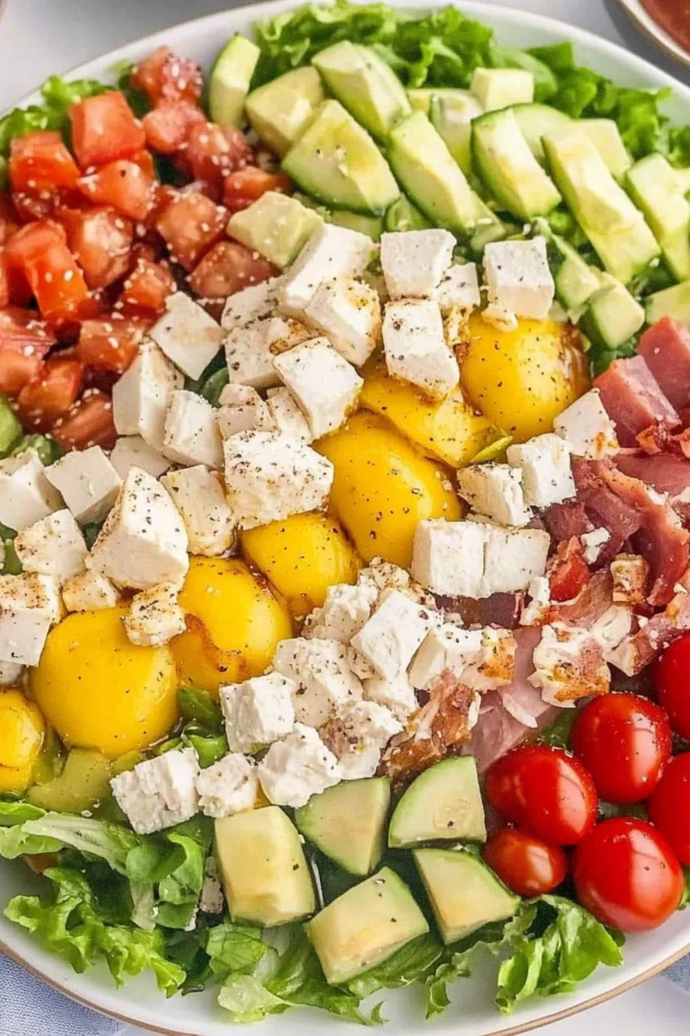 A close-up of a Classic Cobb Salad with fresh greens, cherry tomatoes, diced cucumbers, avocado, crispy bacon, crumbled feta cheese, and hard-boiled eggs, arranged in colorful sections.