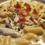 A comforting bowl of creamy chicken pasta soup with tender pieces of chicken, pasta, and crispy bacon bits, topped with fresh parsley for garnish.