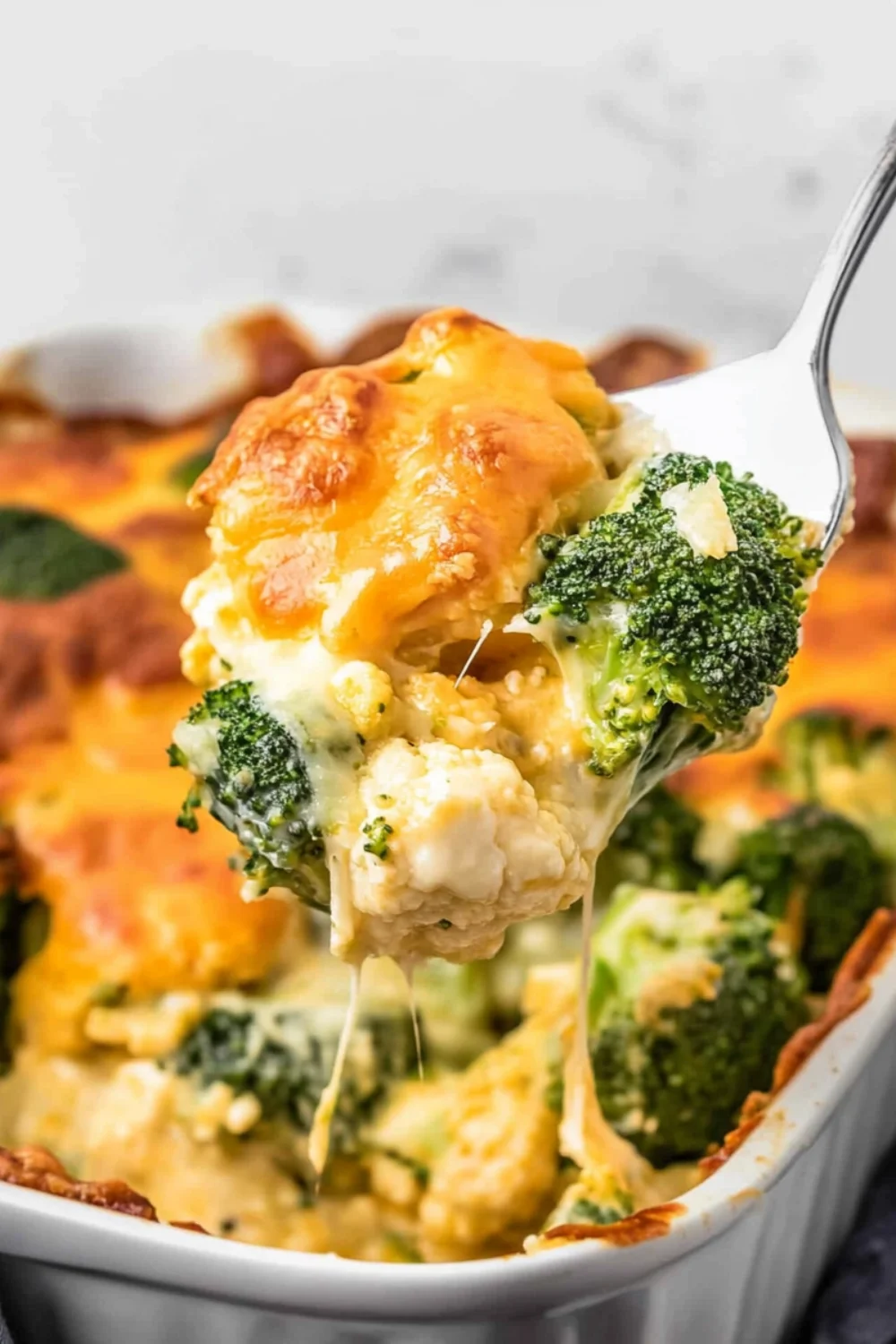 A close-up of Broccoli Cauliflower Casserole being served with melted cheese stretching from the dish, showing vibrant green broccoli, creamy cauliflower, and a golden, bubbly cheese topping.