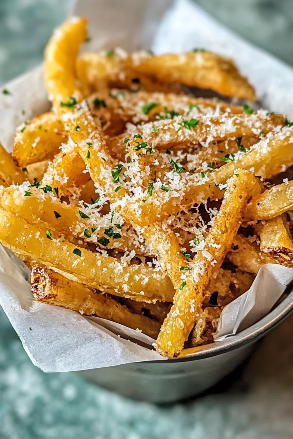 A close-up of Truffle Parmesan Fries garnished with finely grated parmesan and fresh parsley, served in a paper-lined basket.