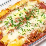 A delicious dish of stuffed manicotti pasta filled with meat and covered with mozzarella cheese, baked in marinara sauce, and garnished with fresh parsley.