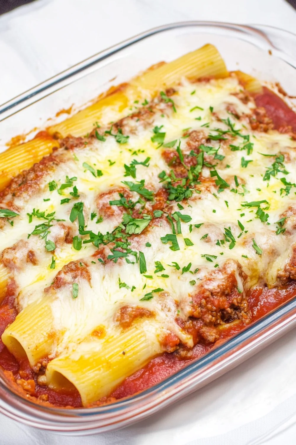 A delicious dish of stuffed manicotti pasta filled with meat and covered with mozzarella cheese, baked in marinara sauce, and garnished with fresh parsley.