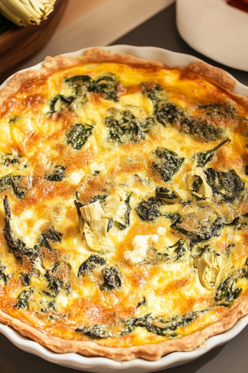 A close-up image of a Spinach, Artichoke, and Goat Cheese Quiche showcasing a golden-brown crust filled with a creamy filling of spinach, artichokes, and crumbled goat cheese.