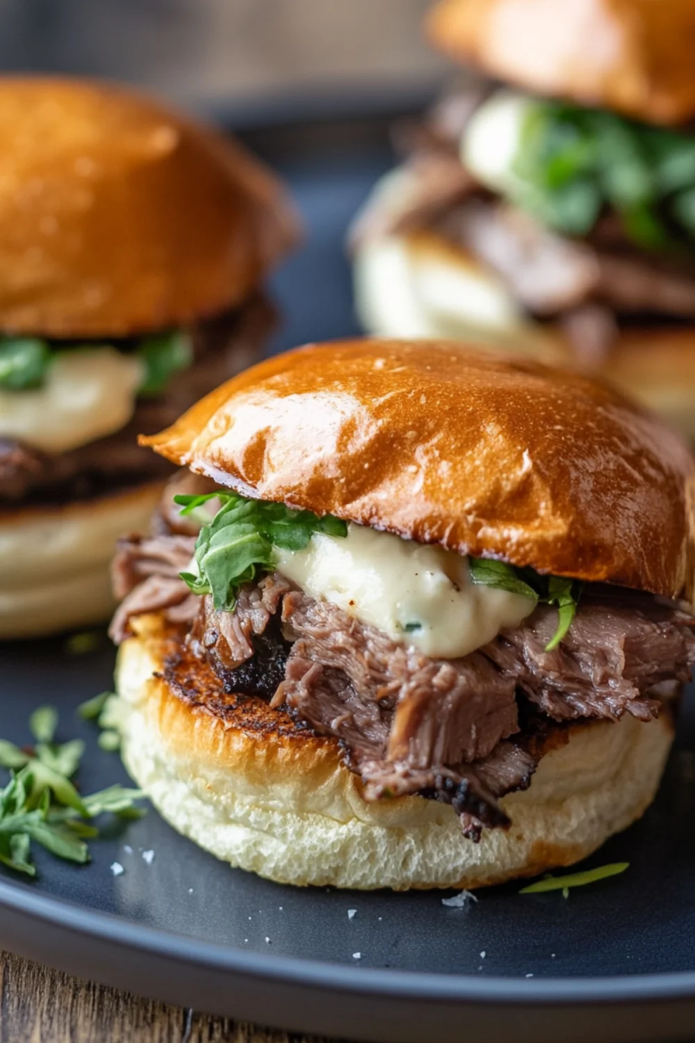 A close-up of Roast Beef Sliders on a plate, featuring tender roast beef, melted cheese, and fresh greens in a toasted bun.