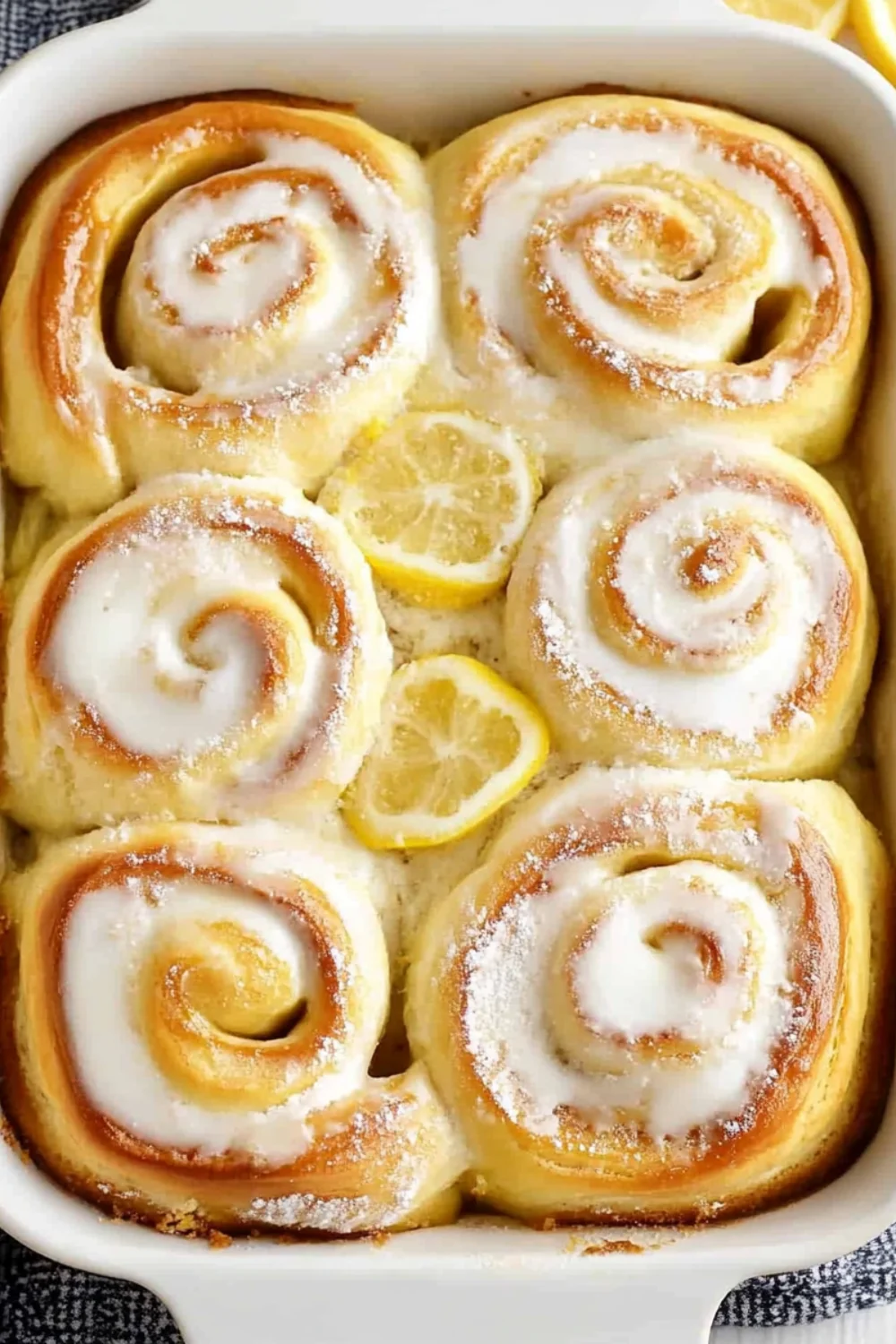 Golden, fluffy lemon sweet rolls topped with a sugary glaze and garnished with lemon slices.