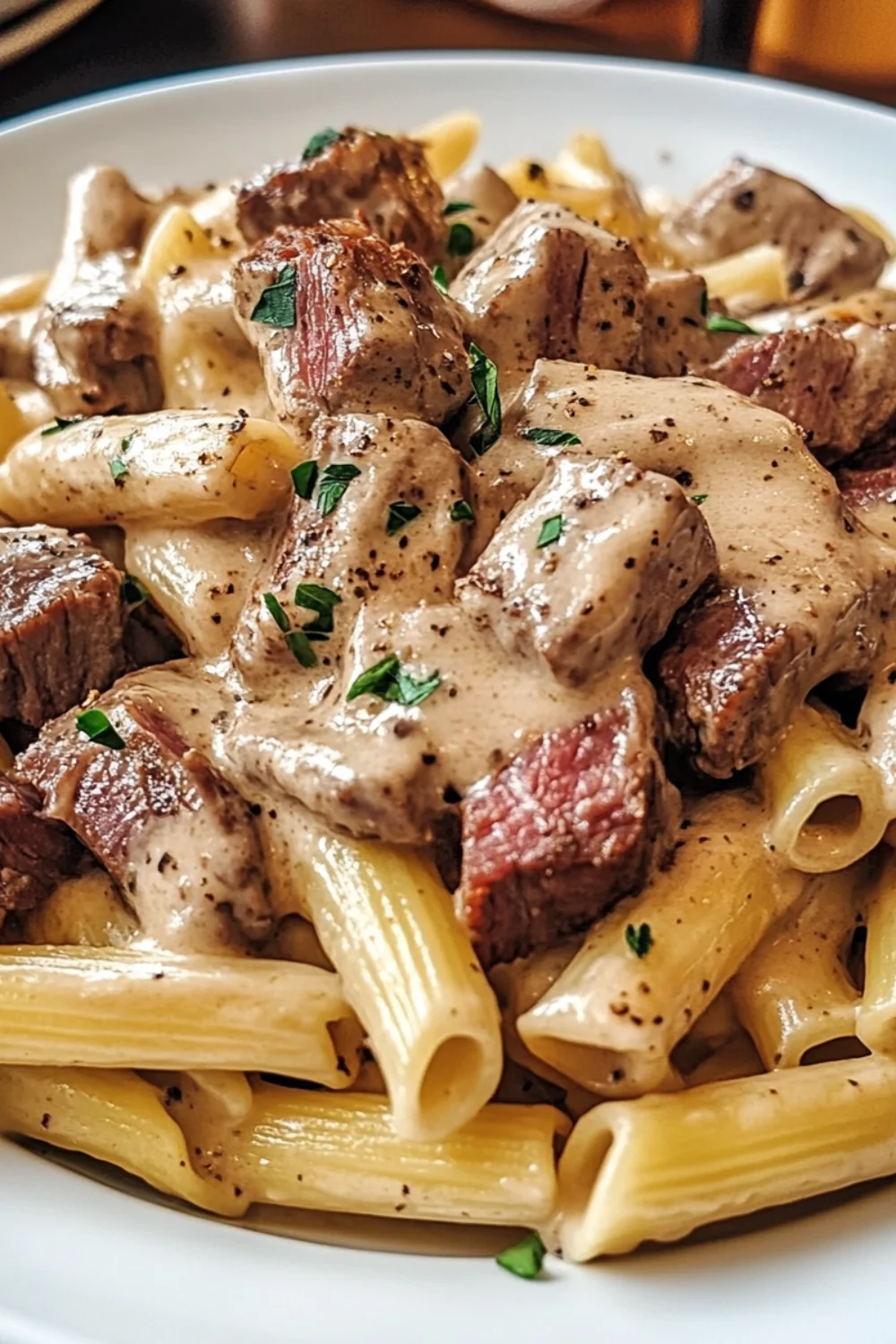 Close-up of creamy steak pasta with tender beef chunks in a rich peppered cream sauce over rigatoni noodles.