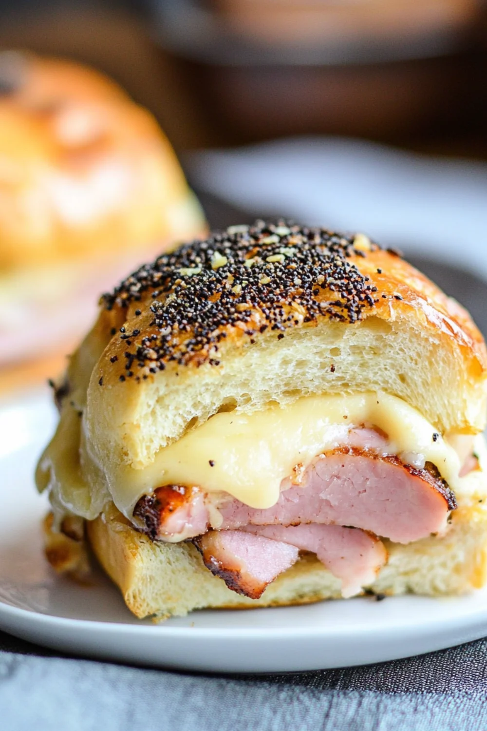 Warm ham and melted cheese slider topped with poppy seeds on a soft golden bun, served on a white plate.