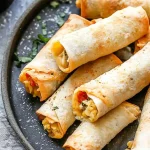 Plate of crispy breakfast taquitos filled with scrambled eggs, cheese, and vegetables, with a side of salsa.