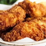 Close-up of crispy golden Southern fried chicken pieces served on a rustic white plate with a napkin underneath.