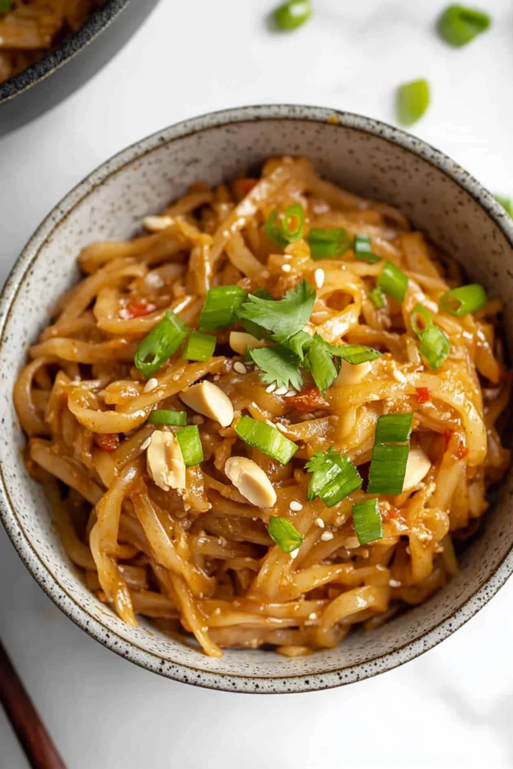 Bowl of spicy peanut butter noodles topped with green onions, cilantro, crushed peanuts, and sesame seeds.